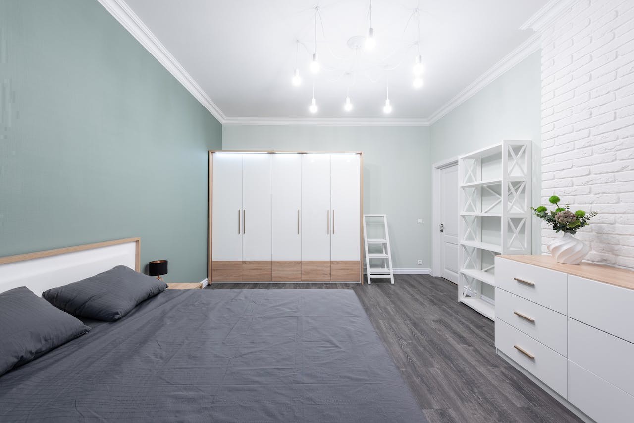 A bedroom in a basement with white furniture and a green wall.